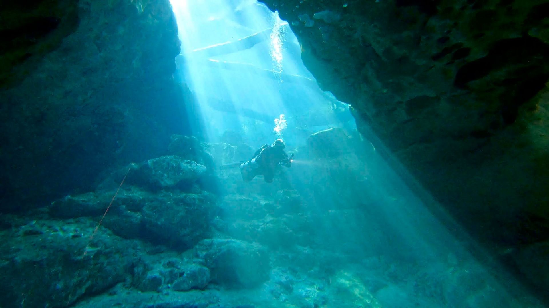 Scuba diver exploring an underwater cave with shafts of sunlight piercing through the water from above.