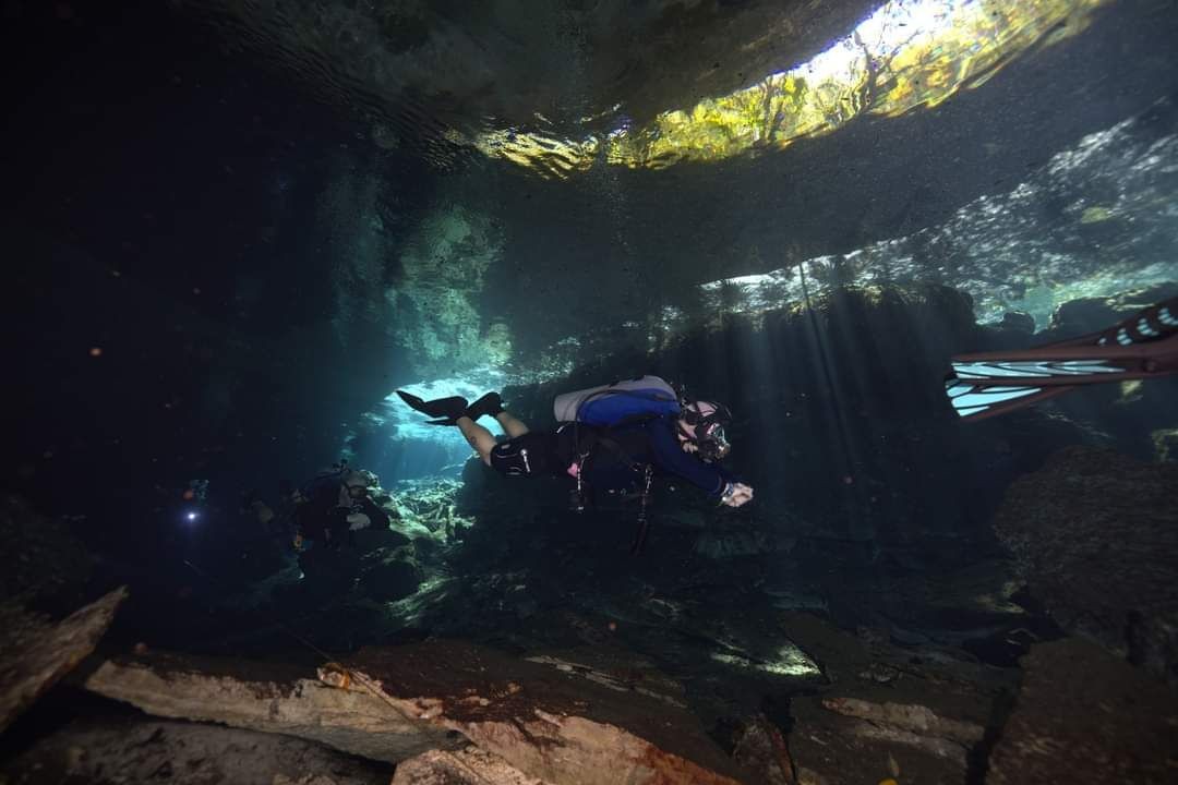 Scuba diver exploring an underwater cave with sunlight filtering through the water.