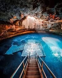 Staircase descending into a stunning underground cave pool illuminated by natural light streaming from above.