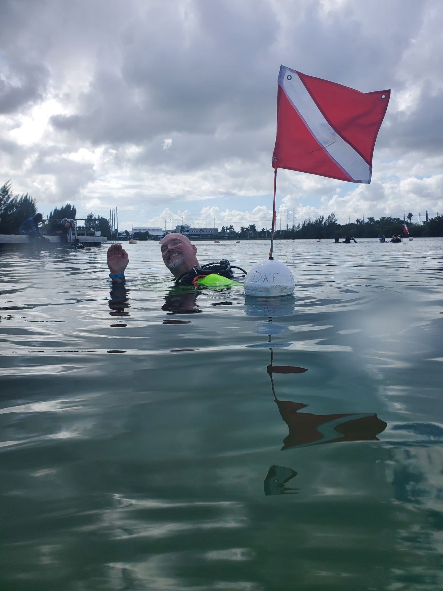 Scuba diver floating in water with a red dive flag, cloudy sky in the background.