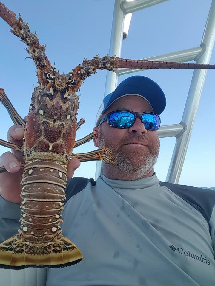 Man holding a large lobster on a boat under a clear blue sky.